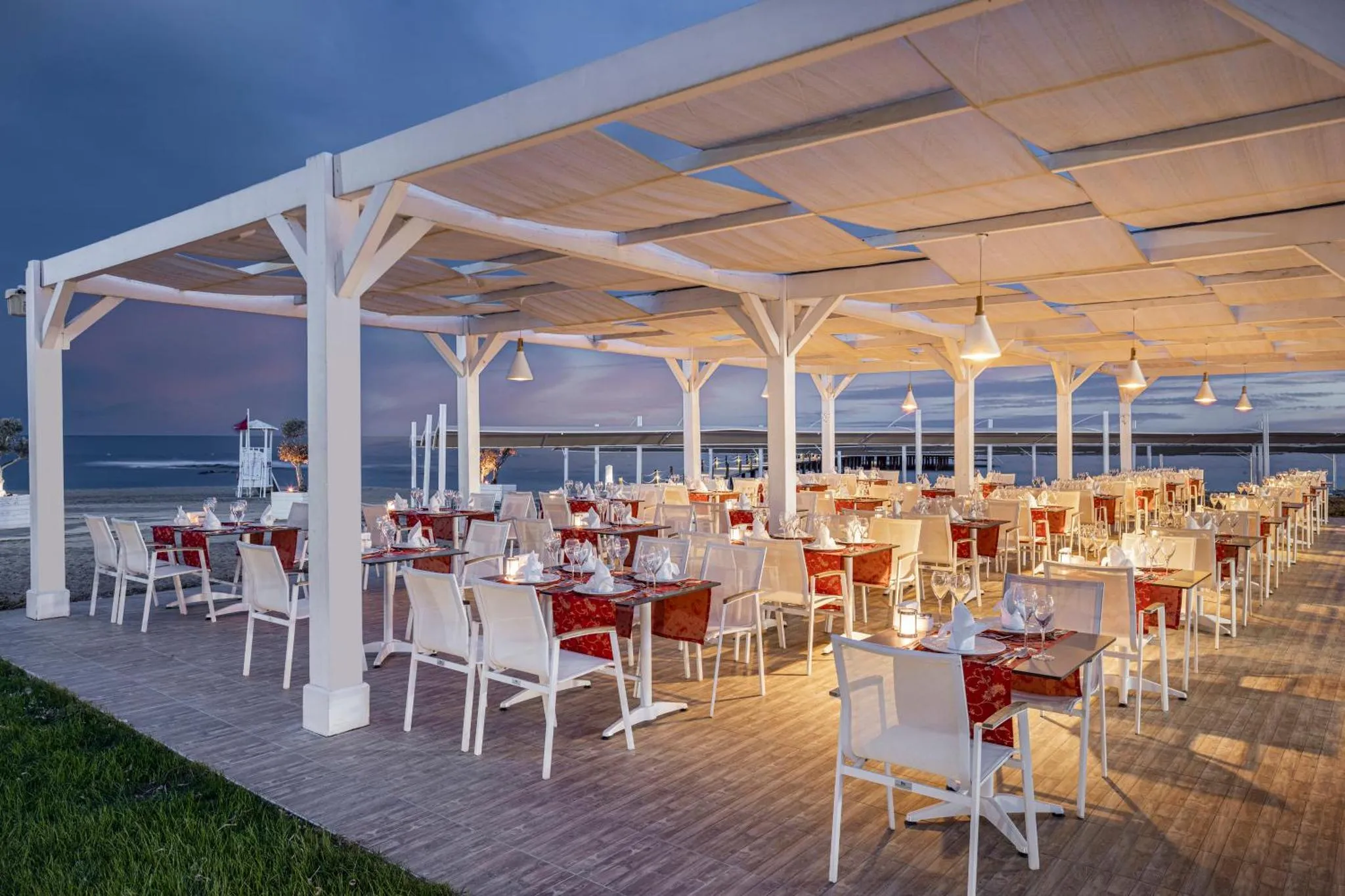 Tables dressées en extérieur sous une pergola lumineuse face à la mer.