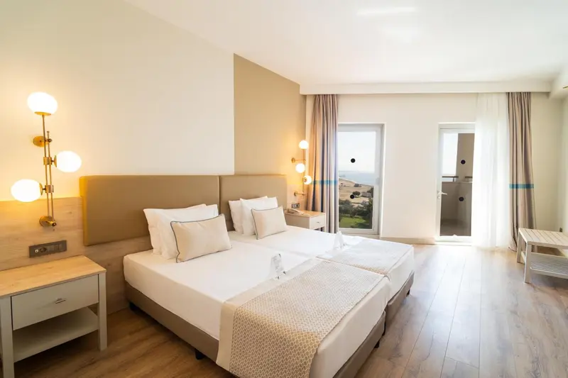 Chambre lumineuse avec deux lits simples et vue sur l'extérieur.