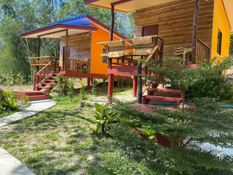 Petites maisons en bois sur pilotis avec terrasses colorées dans un jardin tropical.