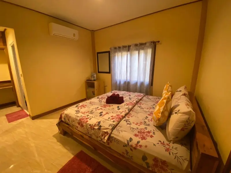 Une chambre lumineuse avec un lit recouvert d'une courtepointe fleurie et un climatiseur mural.