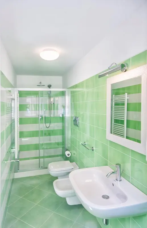 Une salle de bain claire avec douche à l'italienne et carrelage vert.