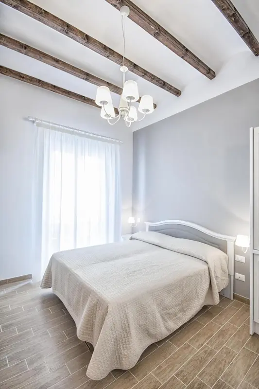 Une chambre lumineuse avec un lit recouvert d'une couverture claire et un plafond avec des poutres apparentes.