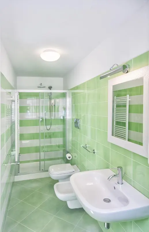 Une salle de bain claire avec douche à l'italienne et carrelage vert et blanc.