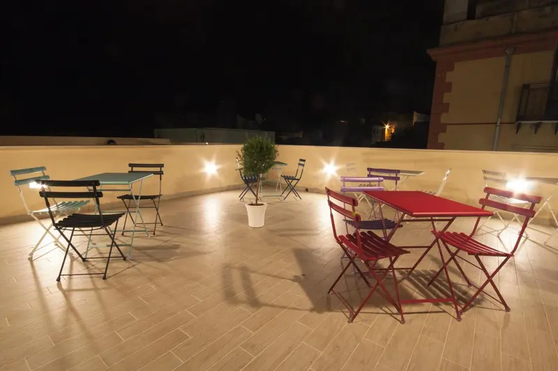 Tables et chaises colorées disposées sur une terrasse éclairée.