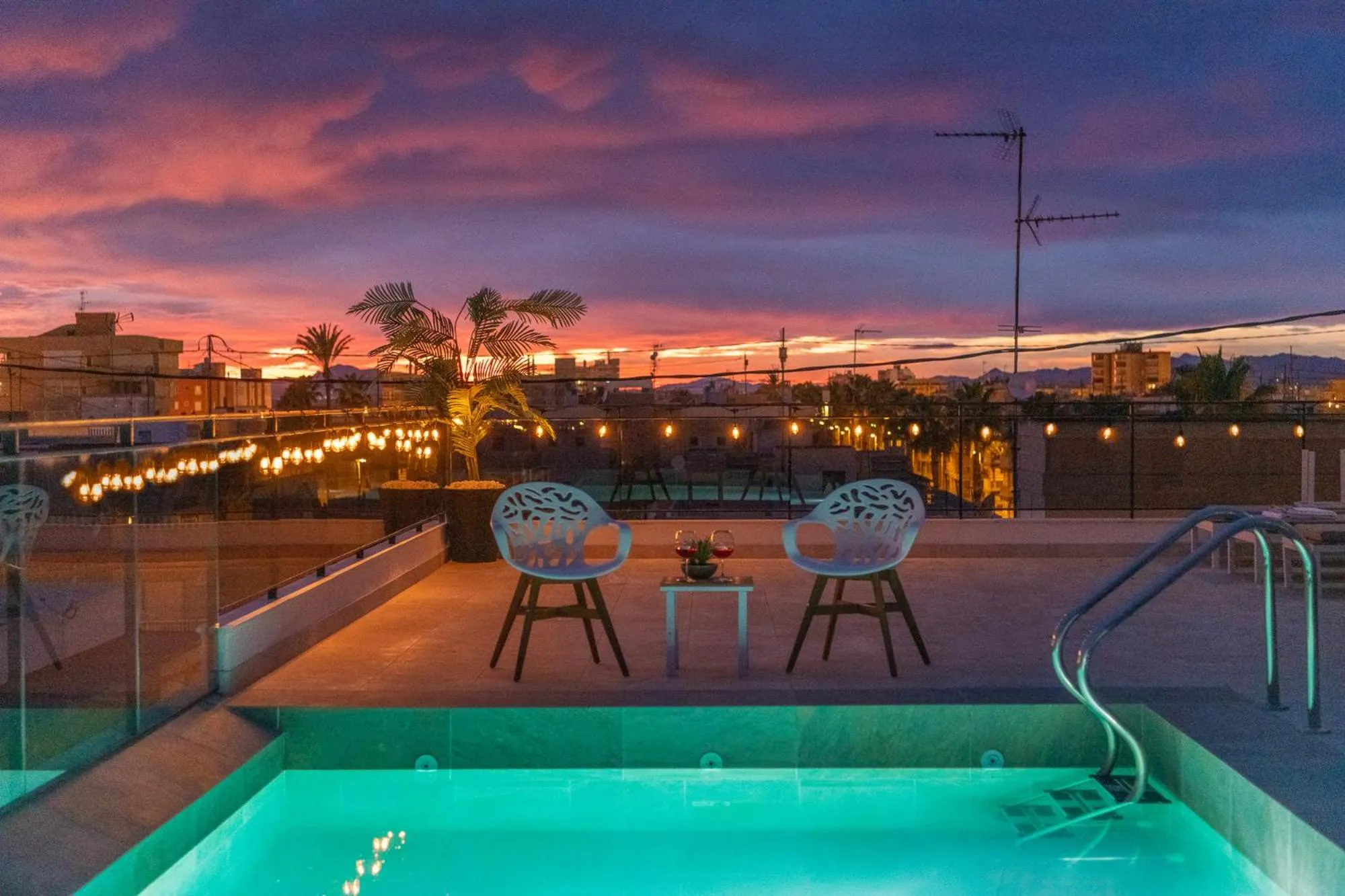 Terrasse avec piscine et mobilier de jardin éclairé au crépuscule.