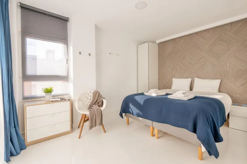 Une chambre lumineuse avec un lit fait et une commode.
