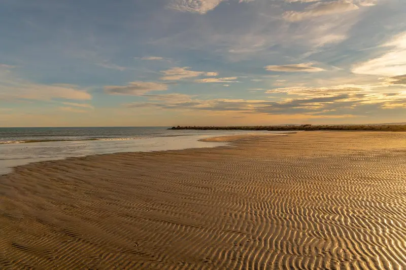 Plage de sable fin baignée par les rayons du soleil couchant.