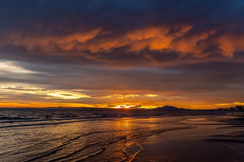 Ciel flamboyant au coucher du soleil sur une plage de sable.