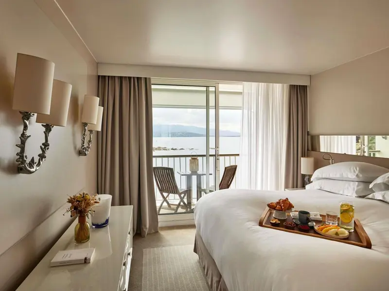 Une chambre lumineuse avec un lit et un plateau de petit-déjeuner, donnant sur une vue mer.