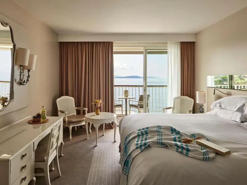 Chambre lumineuse avec un lit et un accès à un balcon donnant sur la mer.