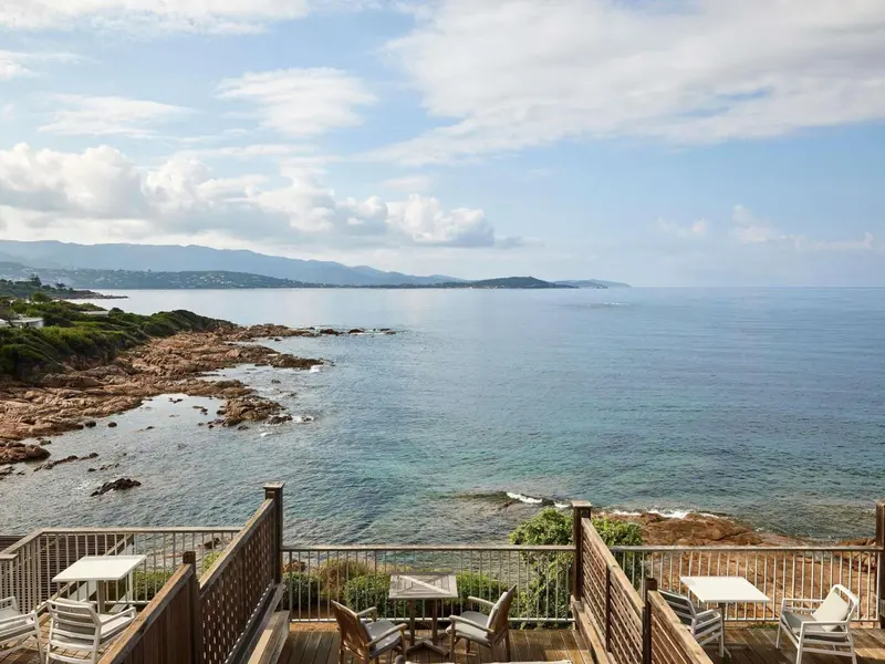 Terrasse en bois avec mobilier de jardin donnant sur la mer et la côte rocheuse.