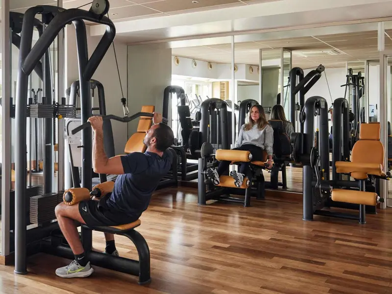 Une salle de sport lumineuse avec des équipements de musculation et des personnes s'entraînant.