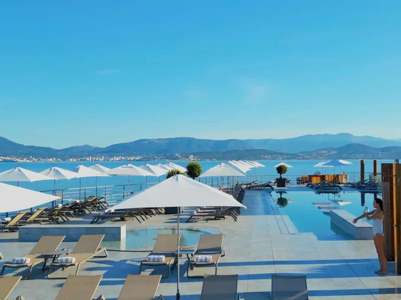 Terrasse avec transats et piscine à débordement offrant une vue sur la mer et les montagnes.