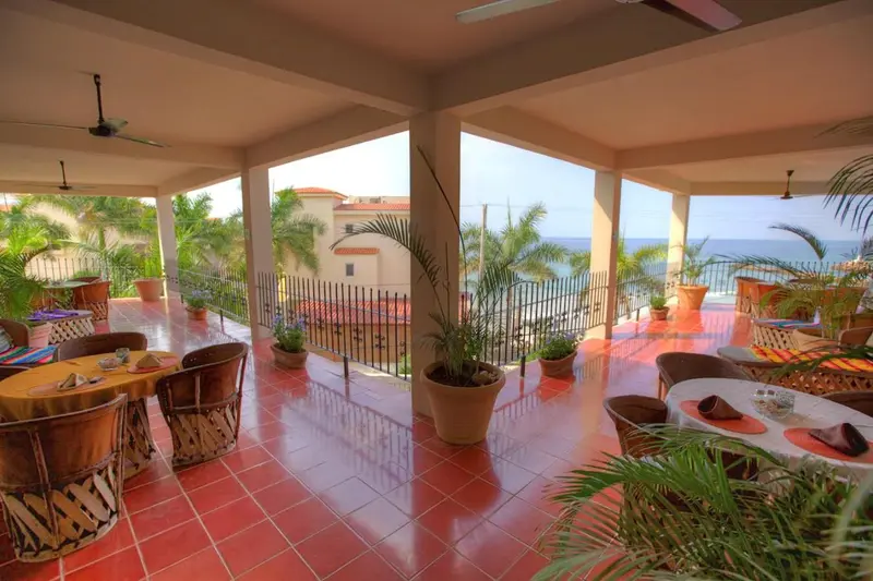 Terrasse ombragée avec tables et chaises, vue sur la mer et la végétation.