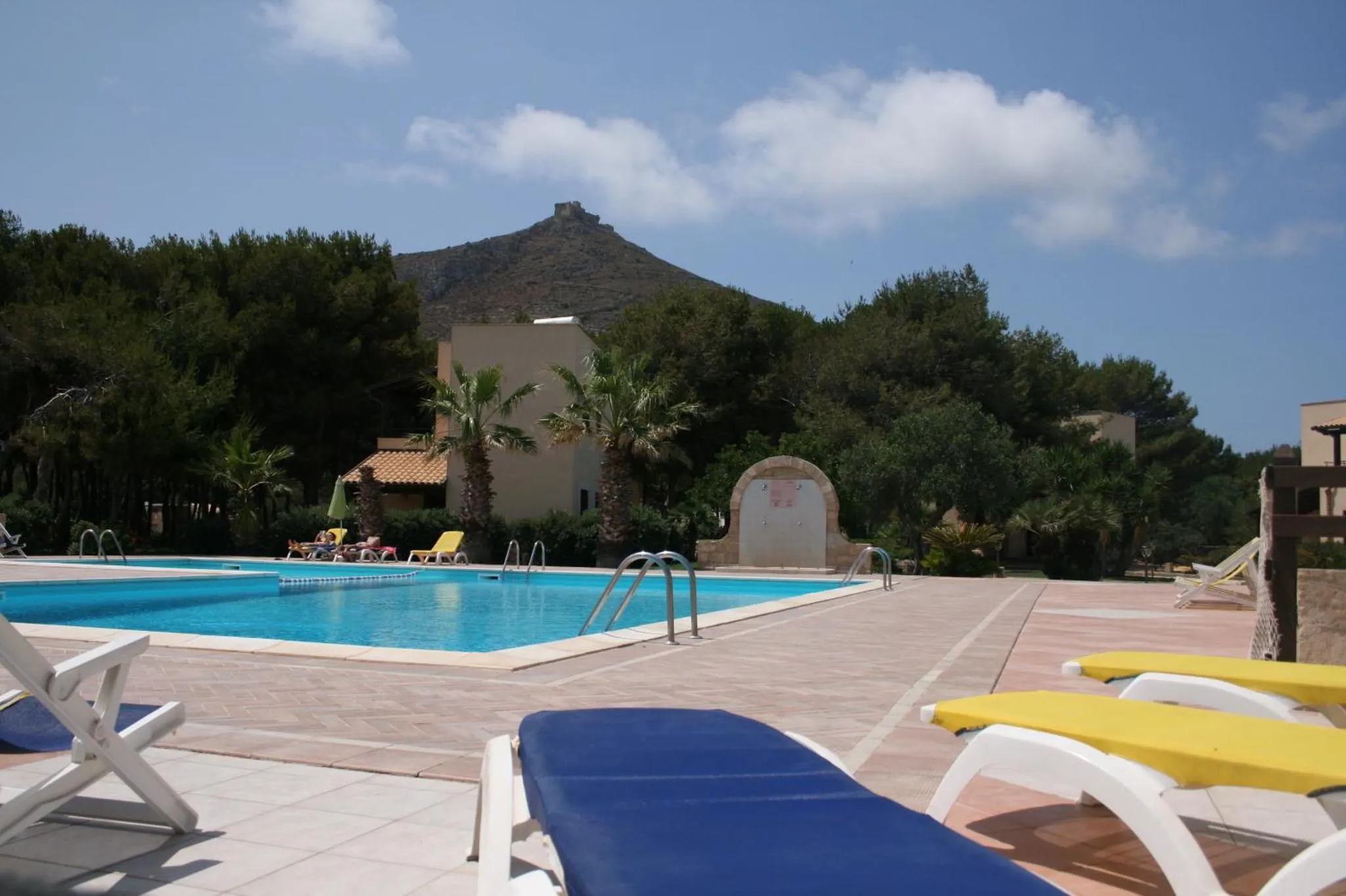 Une piscine turquoise bordée de transats et de palmiers, avec des bâtiments en arrière-plan.