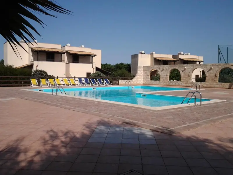 Piscine rectangulaire entourée d'un sol carrelé et de chaises longues.