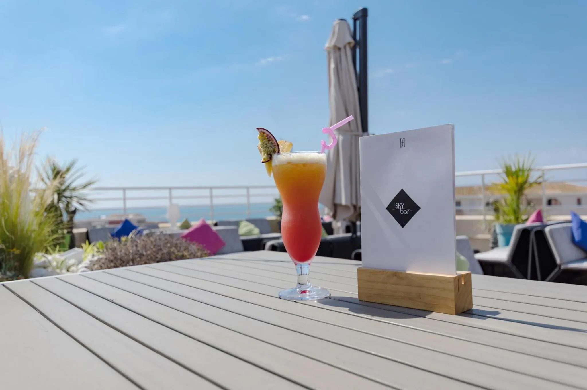 Un cocktail coloré est servi sur une table en terrasse avec vue sur la mer.