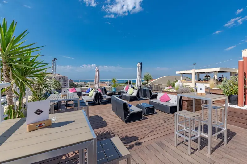 Terrasse aménagée avec tables, chaises longues et parasols offrant une vue sur la mer.