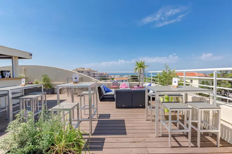 Terrasse aménagée avec tables et chaises, vue sur la mer et le paysage environnant.