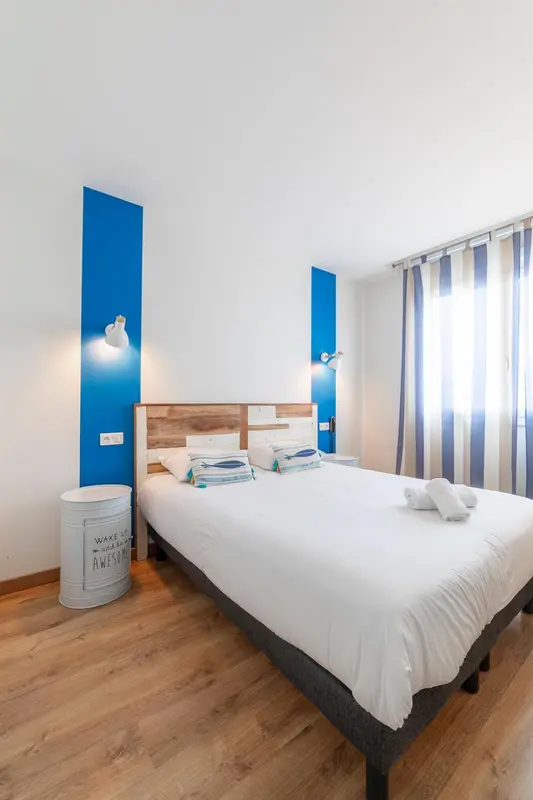 Une chambre lumineuse avec un lit recouvert d'une couette blanche et de coussins bleus.