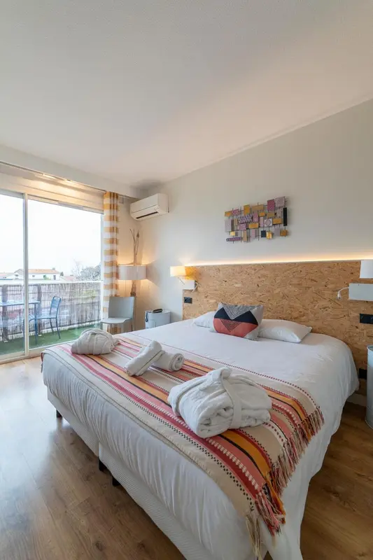 Chambre lumineuse avec un grand lit et une terrasse accessible par une baie vitrée.