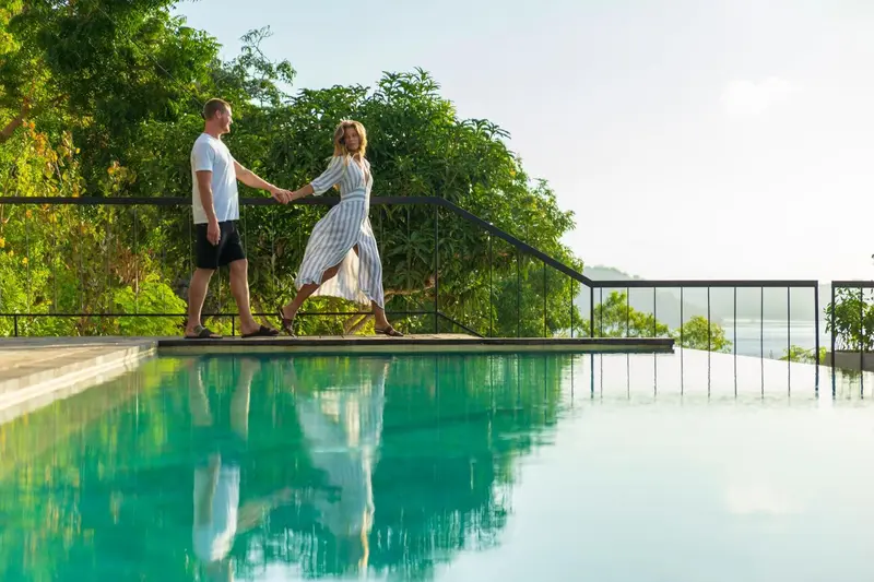 Un couple se promène le long d'une piscine à débordement avec vue sur la mer.