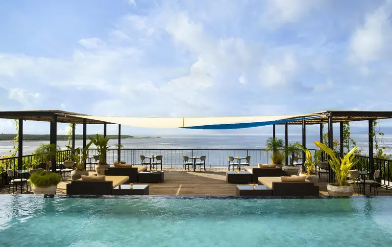 Terrasse aménagée avec salon et tables, surplombant une piscine et la mer.