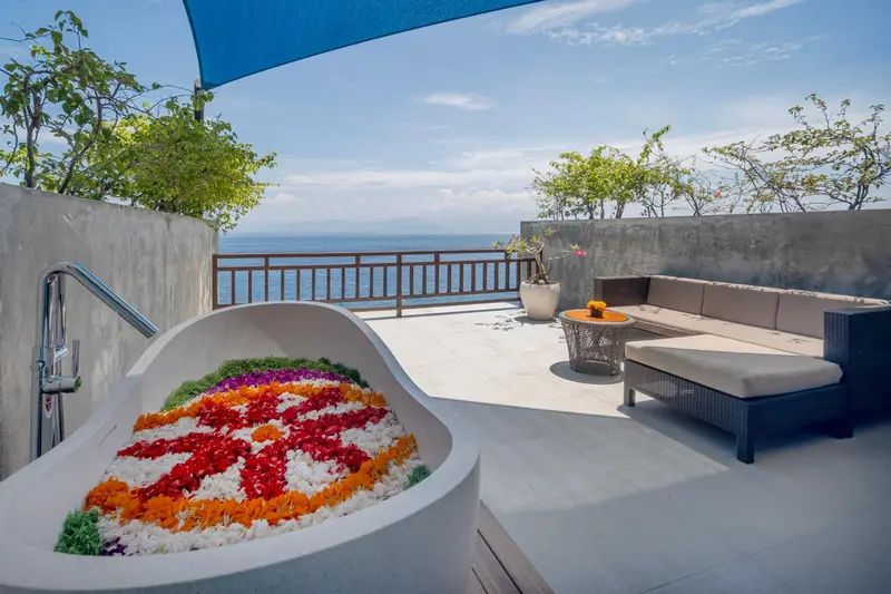 Baignoire extérieure décorée de fleurs sur une terrasse avec vue sur la mer.