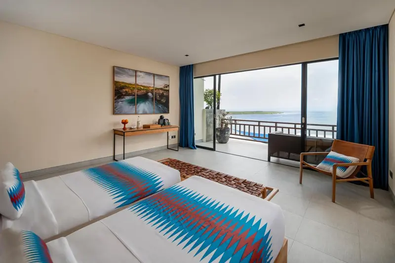 Chambre lumineuse avec deux lits et vue sur la mer.
