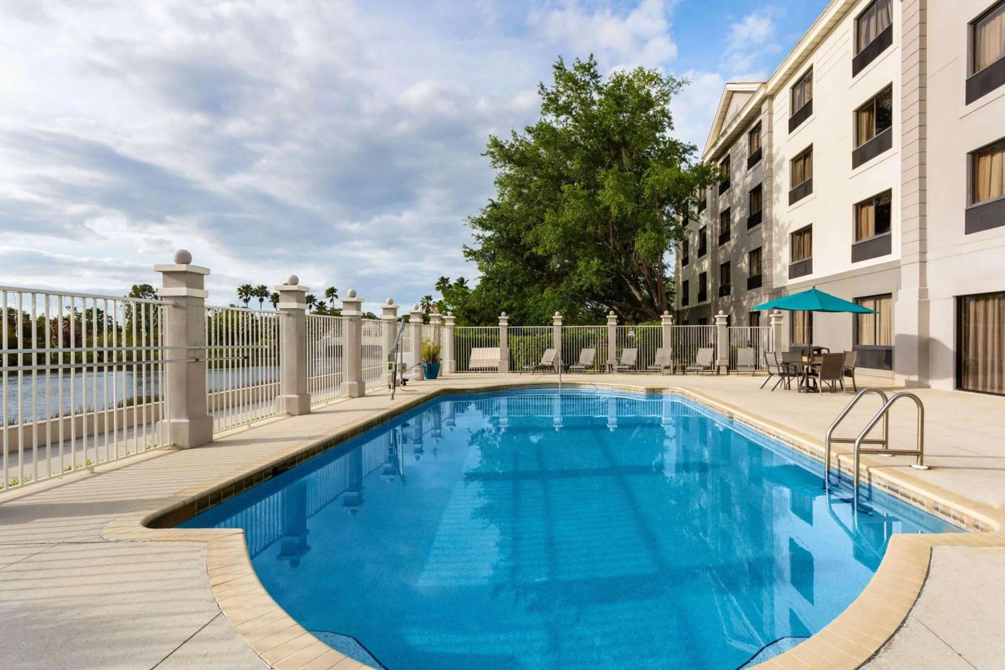 Une piscine bleue bordée d'une terrasse ensoleillée devant un bâtiment.