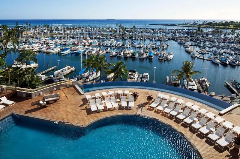 Vue aérienne d'une piscine avec transats surplombant un port de plaisance.