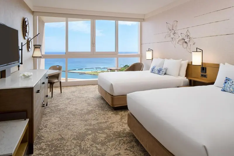 Chambre lumineuse avec deux lits et vue sur la mer.