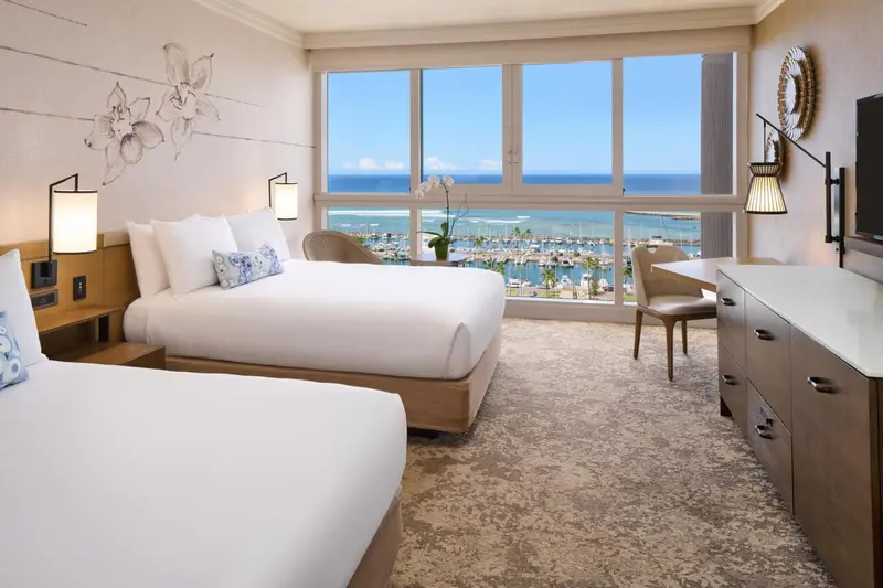Chambre lumineuse avec deux lits et vue sur la mer.