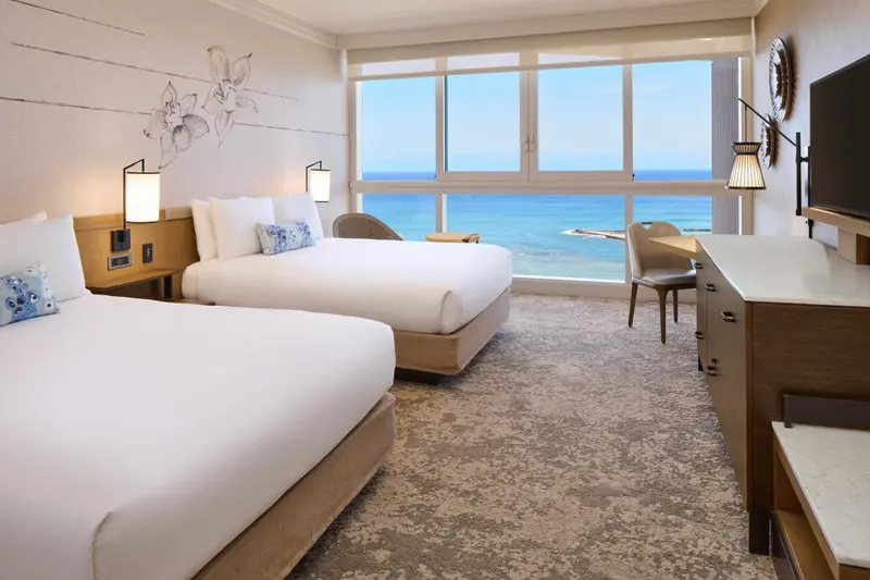 Chambre lumineuse avec deux lits et vue sur la mer.