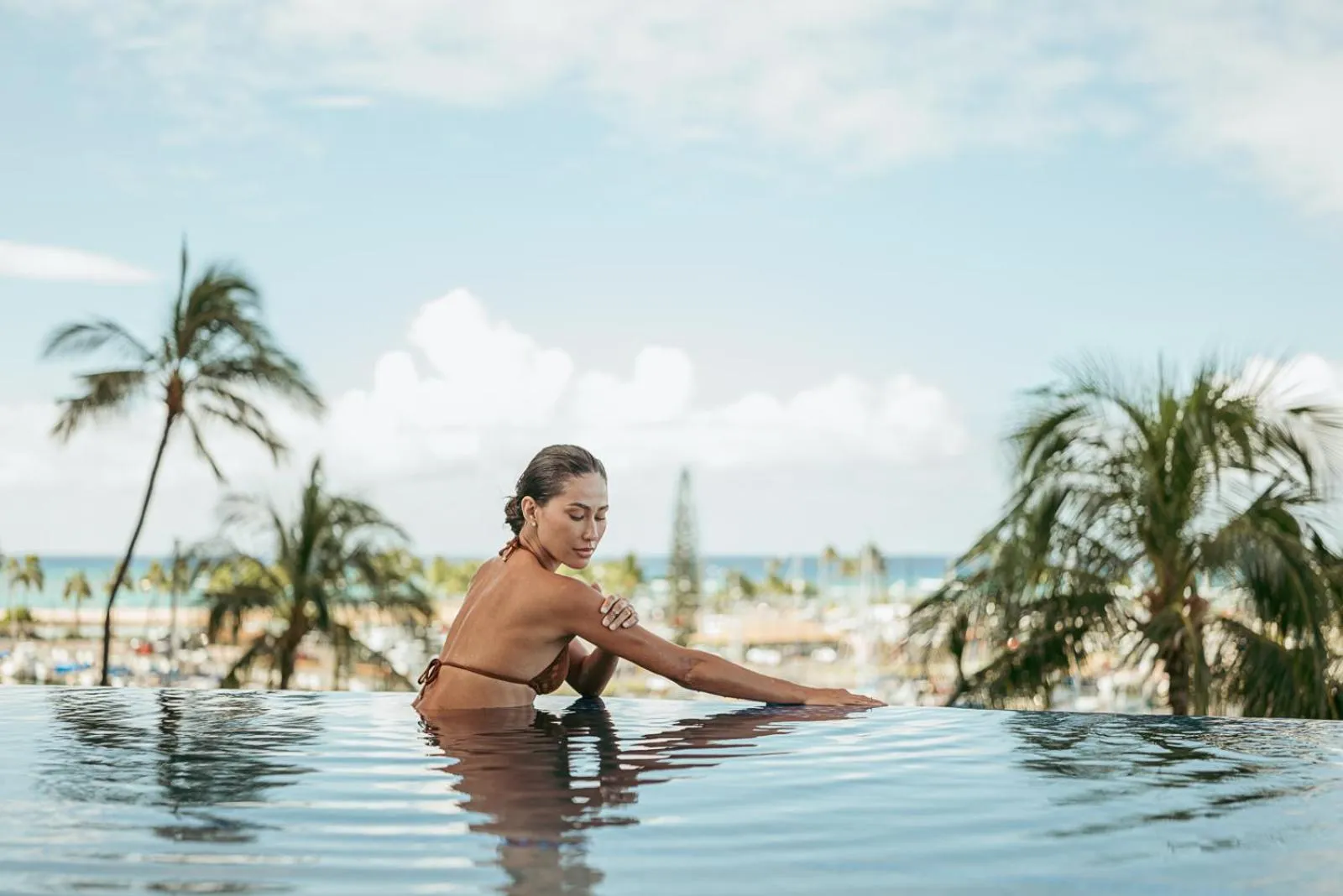 Une femme se détend au bord d'une piscine à débordement avec vue sur la mer et la végétation.