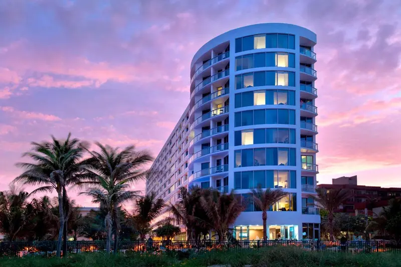 Bâtiment moderne aux nombreuses fenêtres illuminées, vu au coucher du soleil.