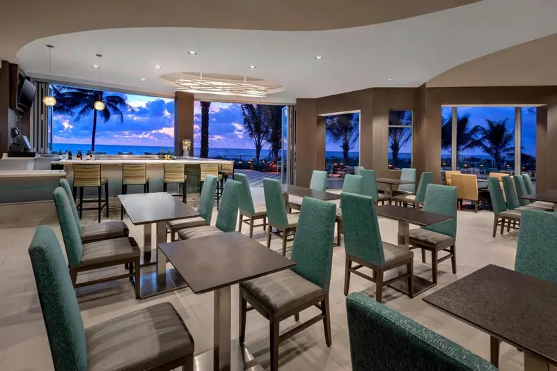 Une salle lumineuse avec un bar et des tables de repas offre une vue sur la mer.