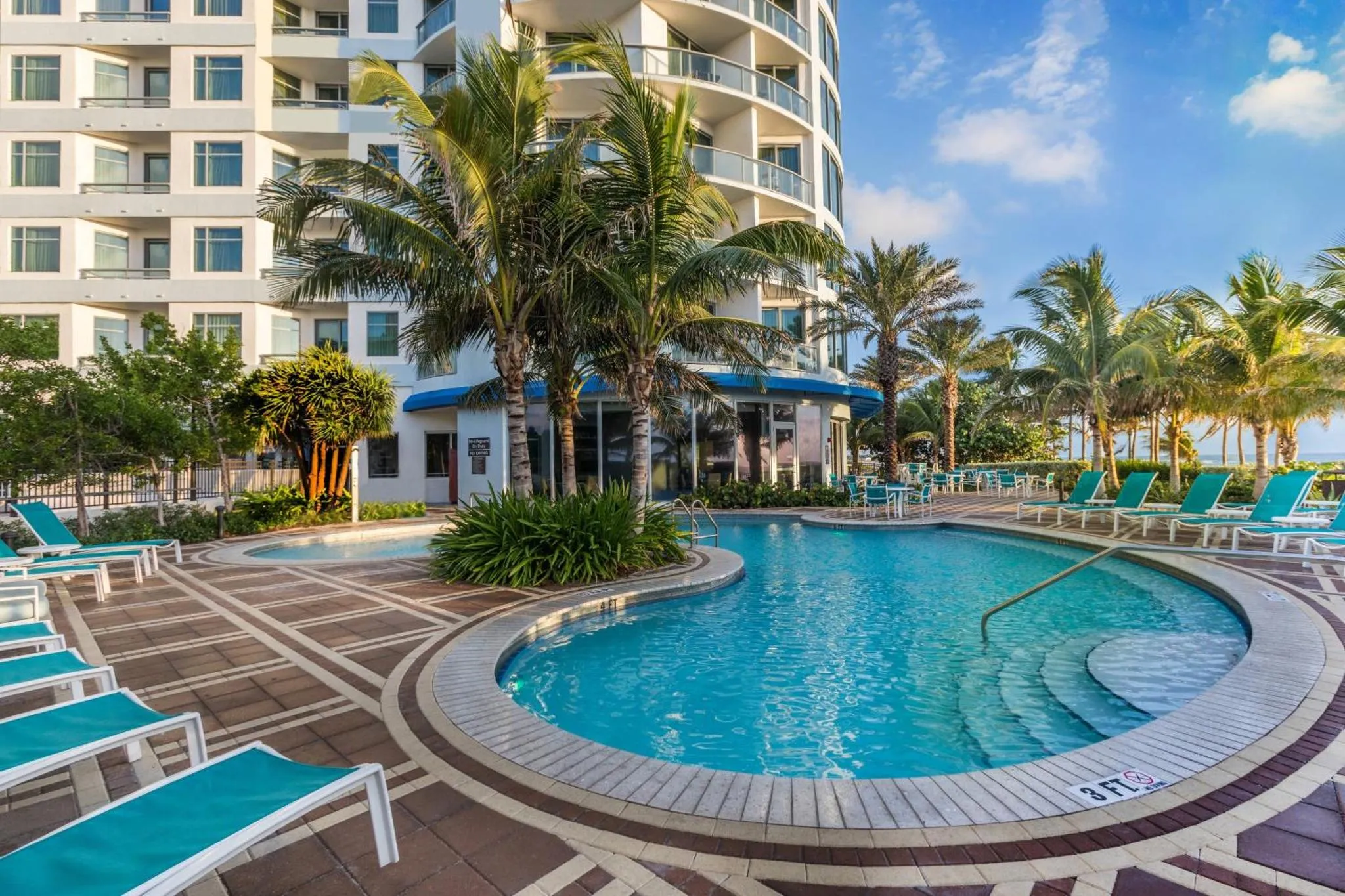 Piscine extérieure avec transats et végétation tropicale devant un bâtiment.
