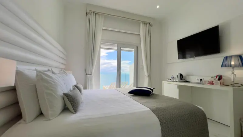 Chambre lumineuse avec un grand lit et vue sur la mer.