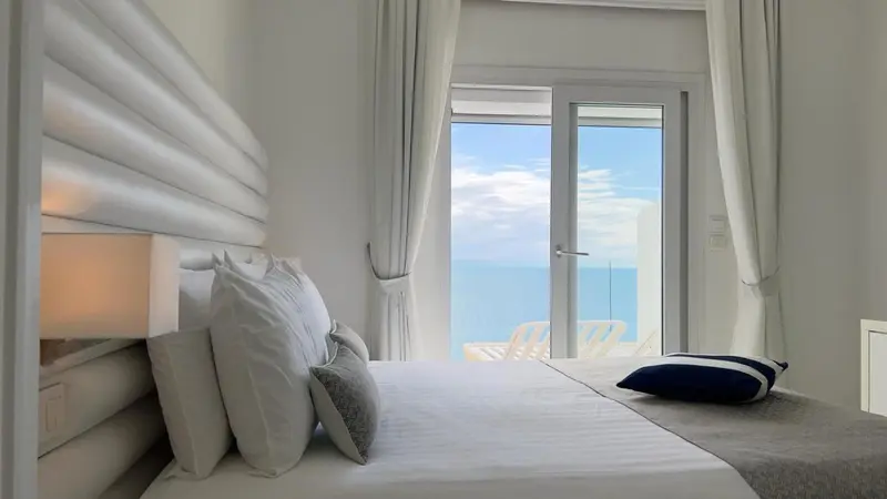 Une chambre lumineuse avec un grand lit face à une baie vitrée donnant sur la mer.