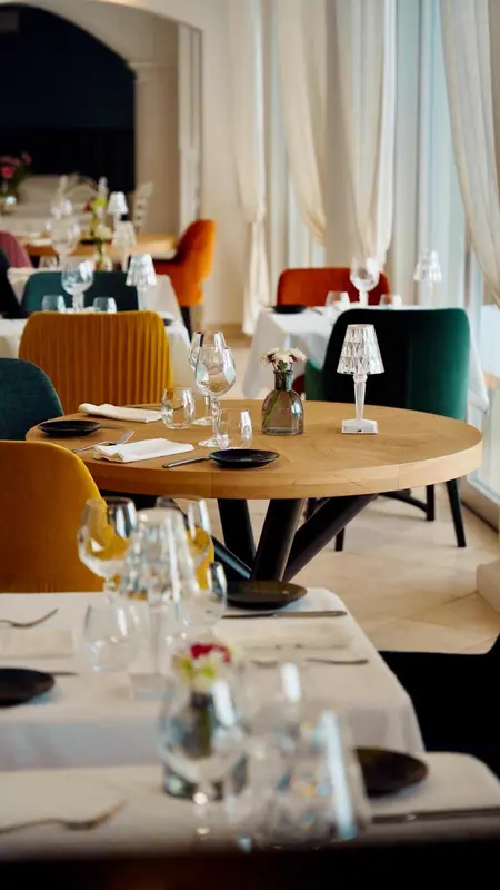 Une salle de restaurant lumineuse avec des tables dressées et des chaises colorées.