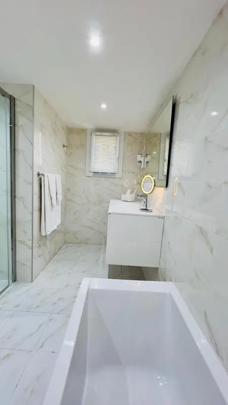Salle de bain moderne avec baignoire et carrelage clair.