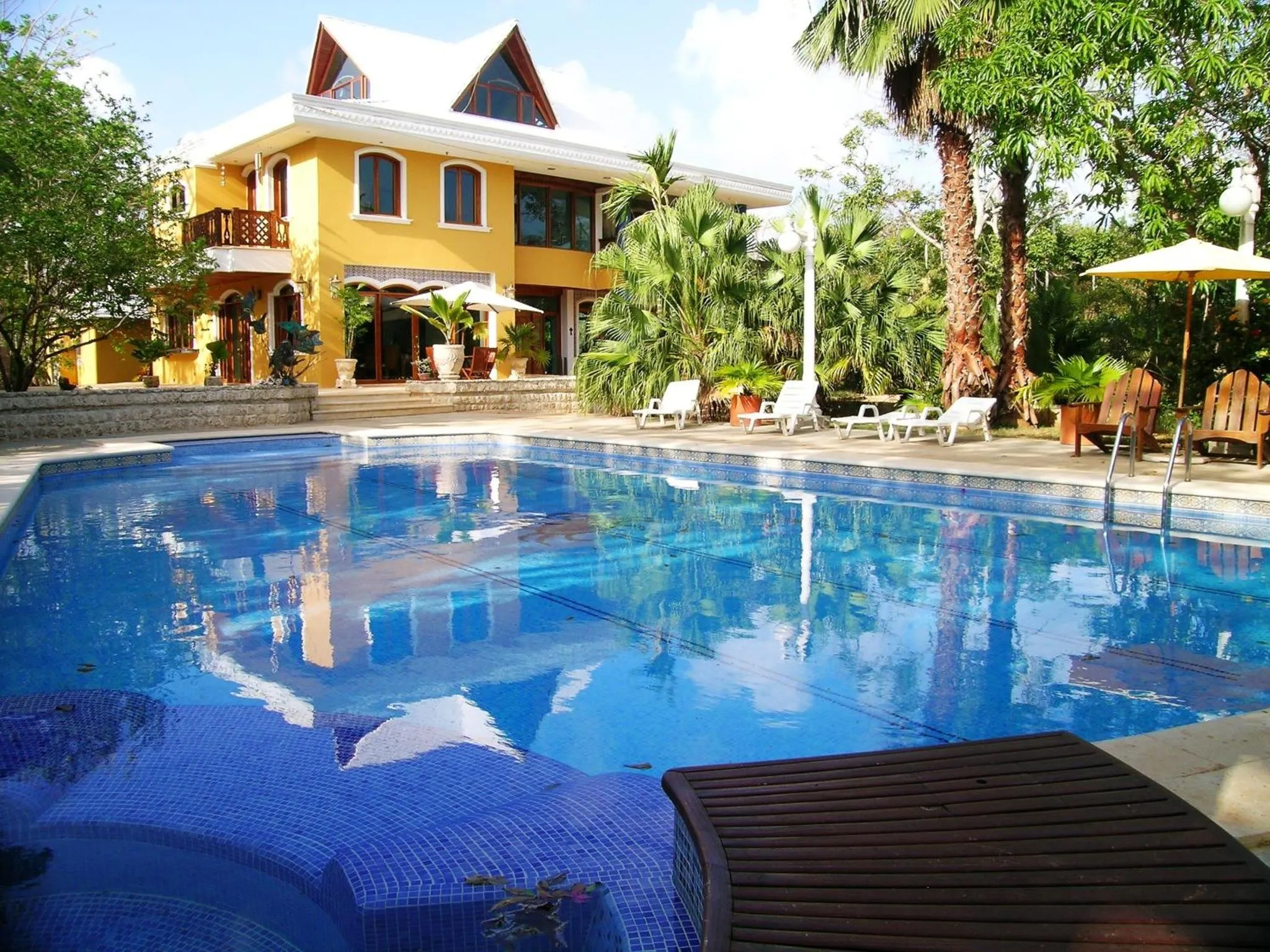 Une piscine turquoise reflète un bâtiment jaune et des palmiers.