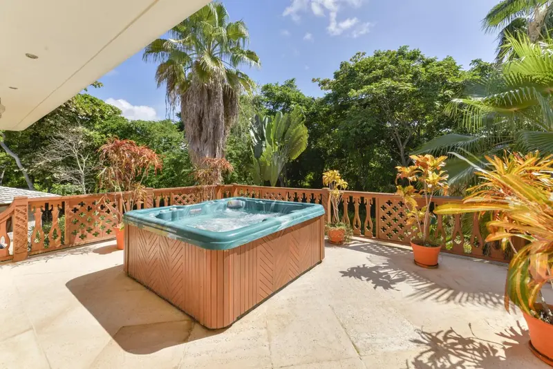 Un jacuzzi extérieur est entouré de végétation tropicale sur une terrasse.