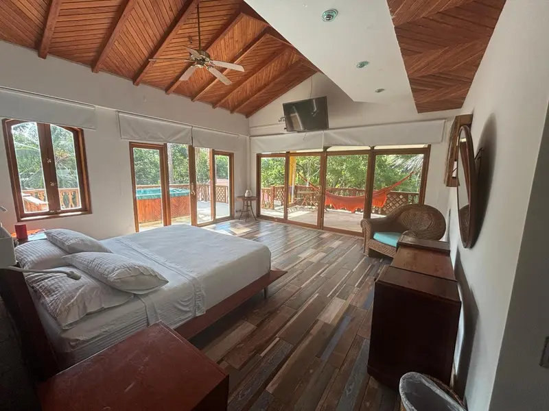Une chambre spacieuse s'ouvre sur une terrasse en bois avec vue sur la végétation.