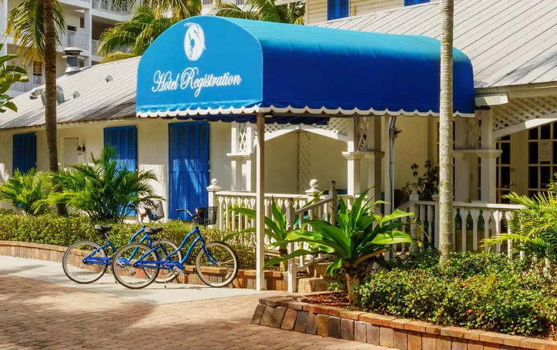 Entrée d'un hôtel ombragée par un auvent bleu et bordée de végétation.