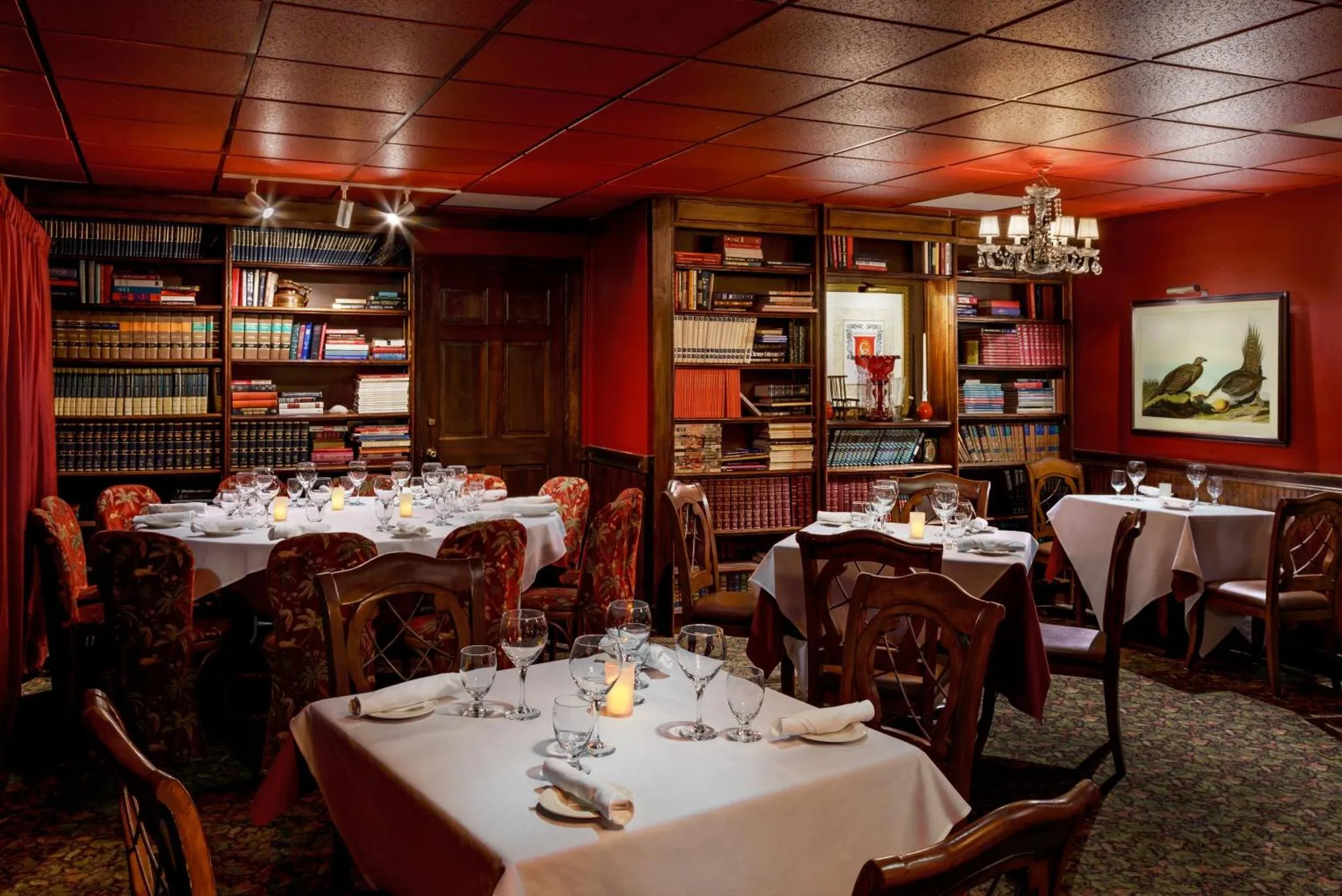 Une salle à manger élégante avec des tables dressées et des bibliothèques en arrière-plan.