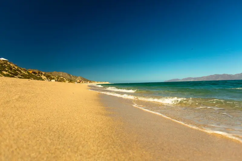 Plage de sable fin bordée par une mer turquoise sous un ciel bleu dégagé.