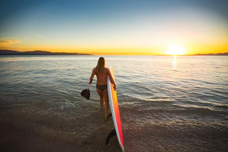 Une personne sort de l'eau avec une planche de surf au coucher du soleil.