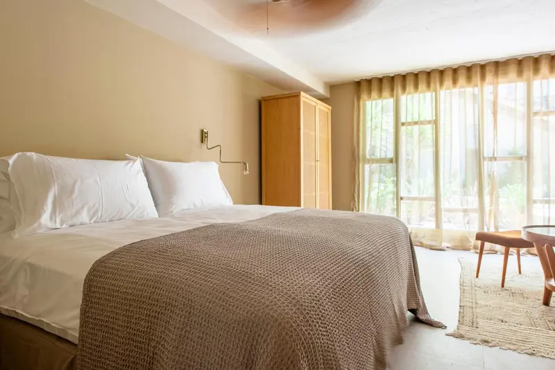 Une chambre lumineuse avec un grand lit et un accès à une fenêtre drapée.